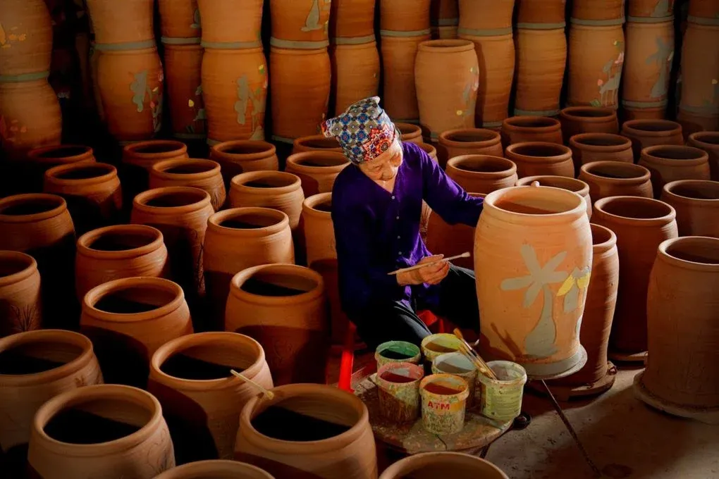 Nghệ nhân làng gốm Phù Lãng đang tỉ mỉ vẽ họa tiết lên chum gốm