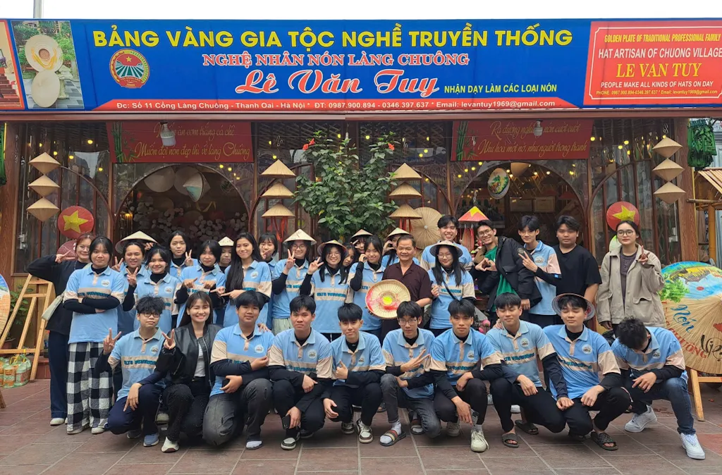Nghệ nhân Lê Văn Tuy (áo nâu) cùng các bạn trẻ tham gia hoạt động trải nghiệm làm nón lá tại làng Chuông