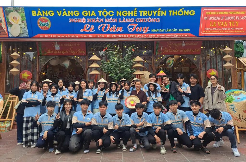 Nghệ nhân Lê Văn Tuy (áo nâu) cùng các bạn trẻ tham gia hoạt động trải nghiệm làm nón lá tại làng Chuông