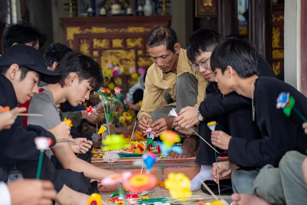 Nghệ nhân Trần Phú (áo vàng) vừa làm hoa, vừa hướng dẫn người trẻ và du khách trải nghiệm nghề truyền thống